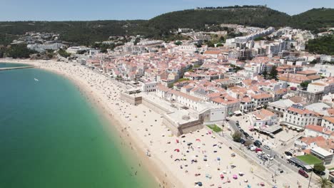 Sesimbra-beach-full-of-tourists-during-vacation,-Aerial-orbital-drone-shot
