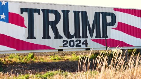 Donald-Trump-2024-Presidential-Election-Campaign-Sign-Painted-on-a-Large-Truck-or-Trailer-in-Rural-Farm-Land-with-Tall-Grass-in-the-Middle-of-Nowhere