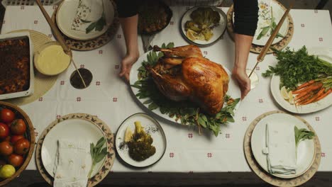 Chef-places-freshly-cooked-big-roasted-turkey-on-plated-and-decorated-thanksgiving-dinner-table
