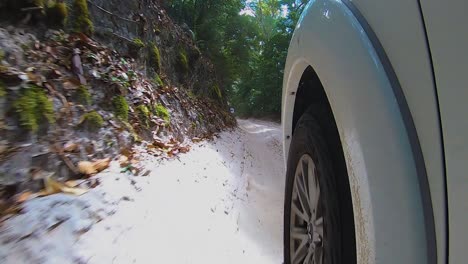 POV-view-past-the-front-wheel-of-a-white-4WD-offroad-truck-from-a-car-mounted-camera,-as-it-bounces-along-a-sandy-inland-trail-through-the-jungle-rainforest-with-steep-sandy-embankments
