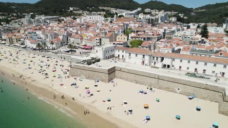 People-relaxing-on-Sesimbra-beach,-Portugal.-Aerial-circling