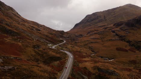 AERIAL---A-winding-road-among-the-mountains,-Glencoe,-Scottish-Highlands,-Scotland