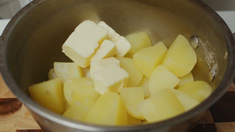 Hinzufügen-Von-Butterwürfeln-Zu-Kartoffeln-In-Einem-Tiefen-Metallkochtopf