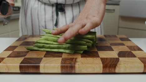 Chef-cuts-greens-with-kitchen-knife-on-a-wooden-cut-board-on-kitchen-table