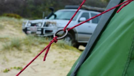 Nice-abstact-shot-featuring-a-close-up-of-a-metal-ring-on-a-tent-guy-rope-at-a-beach-campsite,-with-beautiful-depth-field-and-a-4x4-truck-in-bokeh-in-the-background