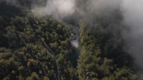 Mountain-road-and-river-passing-through-evergreen-forest-with-mist-in-morning,-aerial