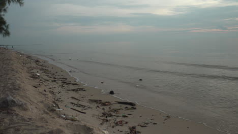 Natural-debris-and-litter-washed-up-on-a-beach-coastline-on-an-early-morning,-the-distant-weather-looking-ominous-with-monsoon-clouds-approaching,-Cha-Am,-Phetchaburi,-Thailand