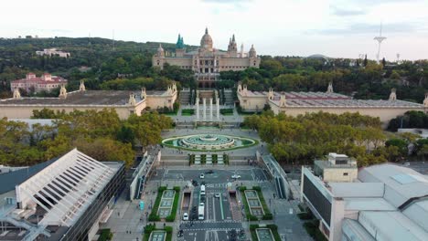 Aerial-view-of-Montjuic-in-Barcelona,-with-tourists-walking-across-an-escalator-footbridge,-the-Magic-Fountain,-the-National-Palace,-and-five-other-palaces