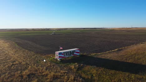 Aerial-Drone-Video-Vote-For-Donald-Trump-2024-Presidential-Election-Campaign-Sign-Painted-on-a-Large-Truck-or-Trailer-in-Rural-Farm-Land-with-Oil-Rig-and-Tall-Grass-in-the-Middle-of-Nowhere