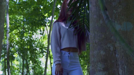 Young-latin-girl-stands-behind-a-palm-branch-before-revealing-her-pretty-face-with-red-hair