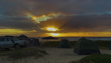 Sunrise-view-over-a-peaceful-beachside-campsite-in-the-dunes-of-Queensland's-Fraser-Island,-with-4x4-truck-and-tents-fluttering-gently-in-the-morning-breeze