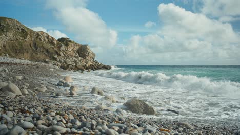 4K-Cinematic-landscape-shot-of-waves-hitting-a-rocky-beach-on-a-sunny-day,-at-Church-Ope,-on-the-island-of-Portland,-in-Dorset,-England