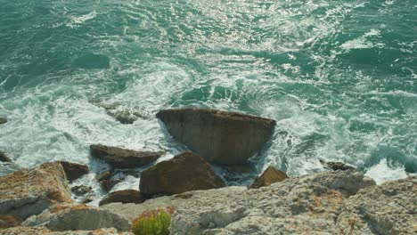 4K-Slow-motion-cinematic-shot-of-big-waves-hitting-rocks-at-the-bottom-of-a-cliff,-on-Portland,-Dorset,-in-England,-on-a-sunny-day