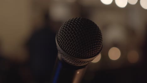 Circular-view-of-a-professional-microphone-on-an-evening-stage-in-a-building-with-blurred-background-and-lights