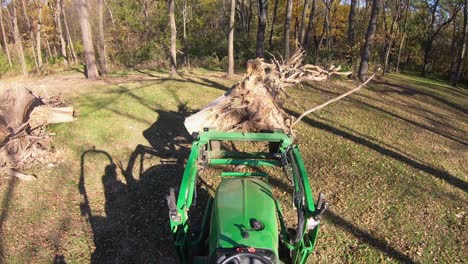 High-angle-point-of-view-on-small-green-tractor-while-using-lift-forks-to-move-a-tree-stump-in-a-clearing-in-the-woods-in-autumn