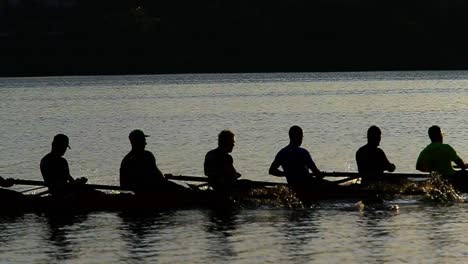 Athletic-male-rowing-team-practising-water-sport-racing-on-lake-water-reflection-at-sunset