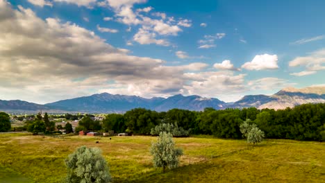 Green-pastures-and-trees-in-a-rural-area-with-cloudscape-above-and-mountains-in-the-background---aerial-hyperlapse