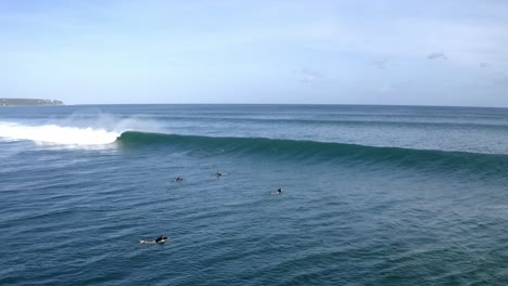 Surfers-at-Balangan-Beach-paddling-to-get-over-a-wave-and-in-deeper-water,-Aerial-hover-shot