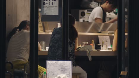 Clientes-Sentados-Frente-A-Un-Chef-Cocinando-En-Un-Restaurante-Japonés-Por-La-Noche-En-Kamata,-Tokio,-Japón