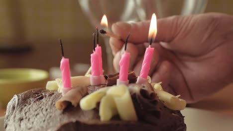 Hand-lighting-candles-on-chocolate-cake-with-match-close-up-shot
