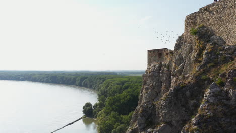 Rotating-side-angle-drone-shot-of-the-Hrad-Devin-castle-with-birds-flying-around-the-cliffs