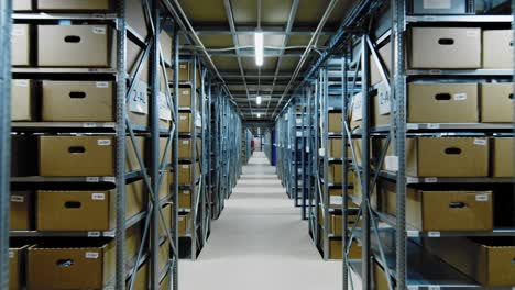 Storage-facility-in-big-warehouse,-racks-filled-with-boxes,-dolly-in