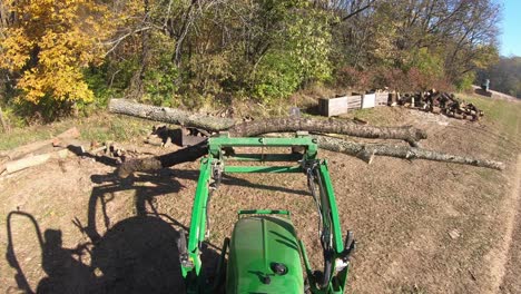 High-angle-point-of-view-on-small-green-tractor-while-using-lift-forks-to-move-logs-to-be-cut-for-a-fireplace