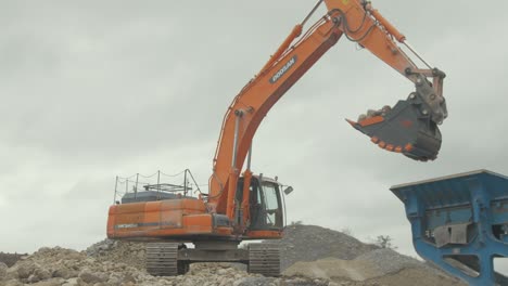 Digger-with-large-bucket-picks-up-stone-filling-rock-conveyor-quarry