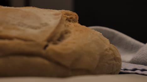 Slow-motion-pan-into-freshly-baked-loaf-of-sour-dough-bread-topped-with-flour-sitting-on-kitchen-bench-with-tea-towel-and-tray,-low-depth-of-field