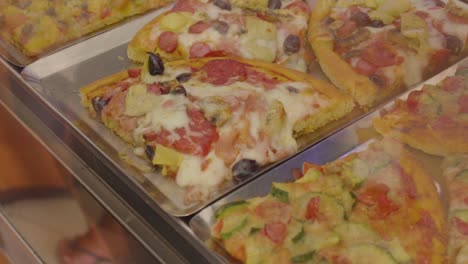 Deliciosas-Rebanadas-De-Focaccia-Y-Pizza-En-Un-Mostrador-De-Panadería-Italiana,-Cámara-Lenta-De-Cerca