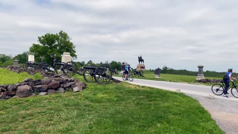 Tourists-on-bicycles-visit-Gettysburg-National-Military-Park,-American-Civil-War-Cannons