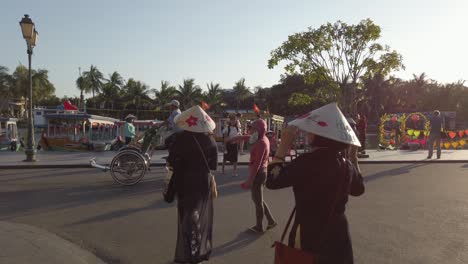Two-women-with-leaf-hats-walking-the-streets-of-the-village-with-cyclo-bicycle-traffic-in-front,-Follow-behind-shot