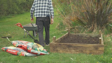 Young-gardener-carries-bag-of-compost-and-drops-beside-raised-garden-bed