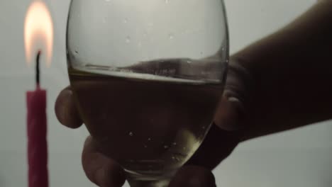 Hand-holding-glass-of-white-wine-silhouette-with-candle-in-background-close-up-shot