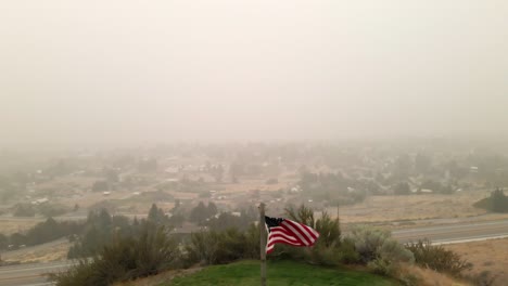 Drone-shot-of-the-United-States-flag-waving-with-the-air-full-of-smoke-in-Wenatchee,-WA-caused-by-West-Coast-fires