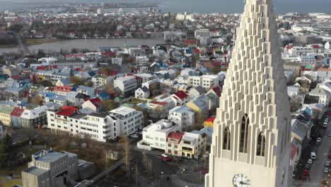 Drone-Flies-Past-Hallgrimskirkja-in-Reykjavík-Cathedral-with-Magnificent-Clock-Tower-revealing-Colorful-City-Rooftops-Behind