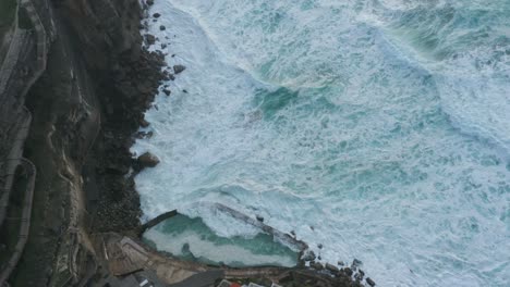 Aerial-Top-Down-View-of-the-waves-crashing-against-the-cliffs-at-Praia-das-Azenhas-do-Mar,-in-Lisbon,-Portugal
