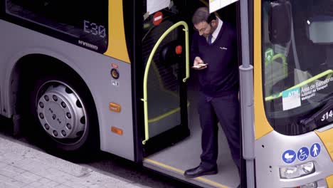 COVID-19:-handheld-close-up-of-a-driver-conductor-checking-his-mobile-standing-at-the-empty-bus-door