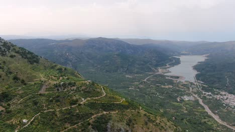 Aerial-of-beautiful-valley-surrounded-by-tall-dense-green-mountains-on-cloudy-day,-Crete