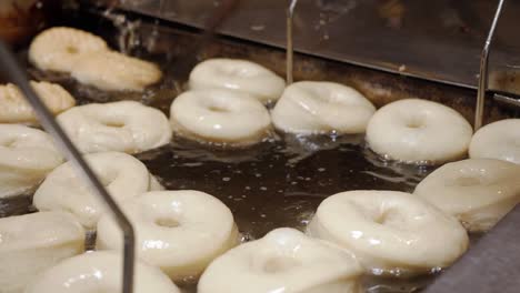 A-cinematic-close-up-of-a-bakers-stick-flipping-a-batch-of-fresh-doughnuts-in-a-homemade-oil-filled-fryer