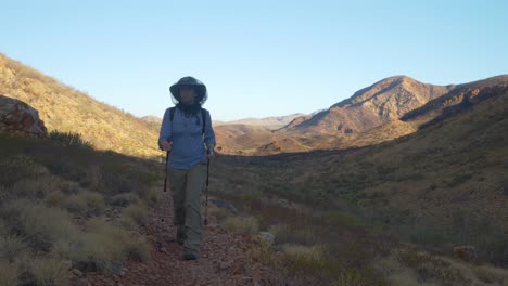 Hiker-walks-towards-camera-in-arid-mountainous-landscape,-Central-Australia