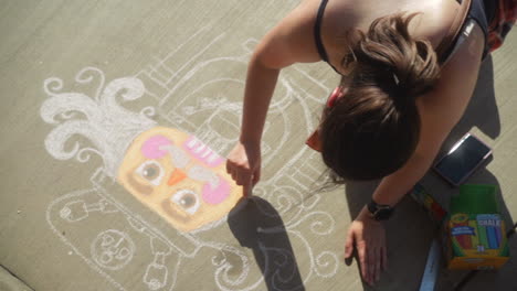 Young-girl-draws-nutcracker-in-chalk-on-sidewalk-during-art-festival,-Pan-Left