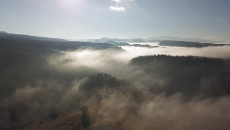 Hochflug-über-Berge-Und-Täler,-Bedeckt-Mit-Weißen-Teppichwolken-Mit-Strahlend-Weißen-Sonnenstrahlen-Im-Hintergrund,-Luftiger-Rückzug-über-Dem-Kopf
