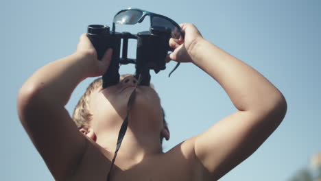 Young-Boy-Using-Binoculars-And-Look-Up-Into-The-Bright-Blue-Sky-On-A-Sunny-Summer-Day