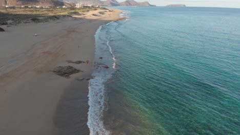 Beautiful-shoreline-summertime-flight-above-turquoise-clear-ocean-sea-water-with-waves-rolling-on-Calheta-sandy-beach-at-sunset,-Portugal,-overhead-aerial-approach