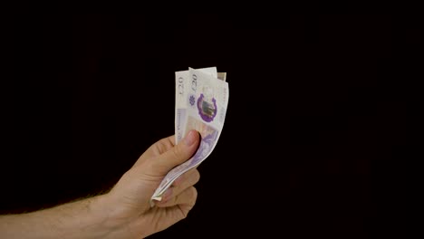 Hand-rubbing-a-neat-stack-of-cash-money-constantly-against-a-black-background-in-slow-motion
