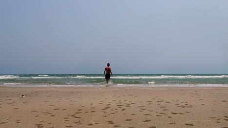 4k-footage-of-a-fit-lone-man-casually-walking-on-an-empty-beach-and-dives-into-the-ocean