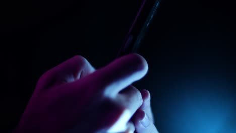 Daumen-Scrollen-Und-Auf-Ein-Smartphone-Tippen-Nahaufnahme-Seitenprofil-In-Einem-Dunklen-Raum-Mit-Violetter-Und-Blauer-Beleuchtung