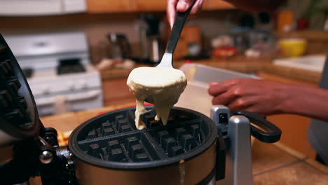 Young-man-making-waffles-for-the-family---spoons-batter-on-the-waffle-iron-in-slow-motion