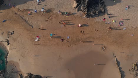 Summer-scene-directly-above-people-walking,-resting,-relaxing-and-enjoying-Calheta-sandy-beach,-coastline,-and-ocean-sea-water-and-waves-at-sunset,-Madeira,-Portugal,-overhead-aerial-static